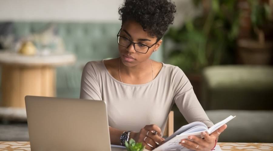Woman studying with laptop and book at desk.
