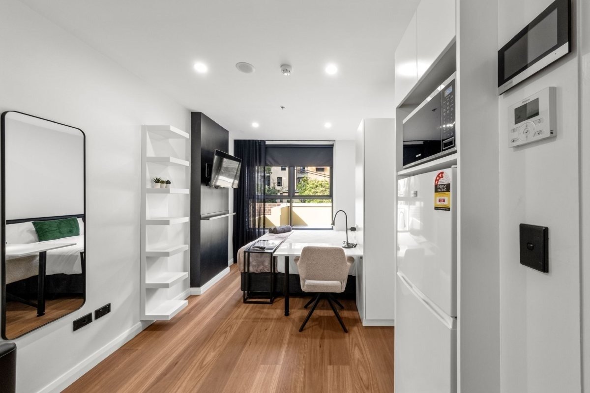 Modern studio apartment with desk and kitchen area.